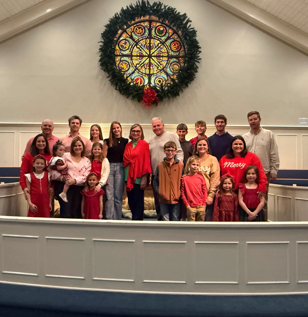 Group photo of people dressed in festive holiday attire inside a church with a large wreath.